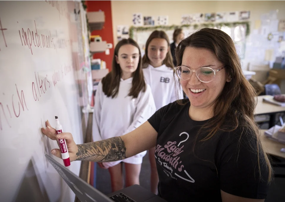 female teacher holding laptop and writing on whiteboard