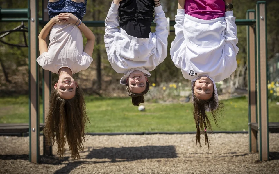 3 students hanging upside down on monkey bars